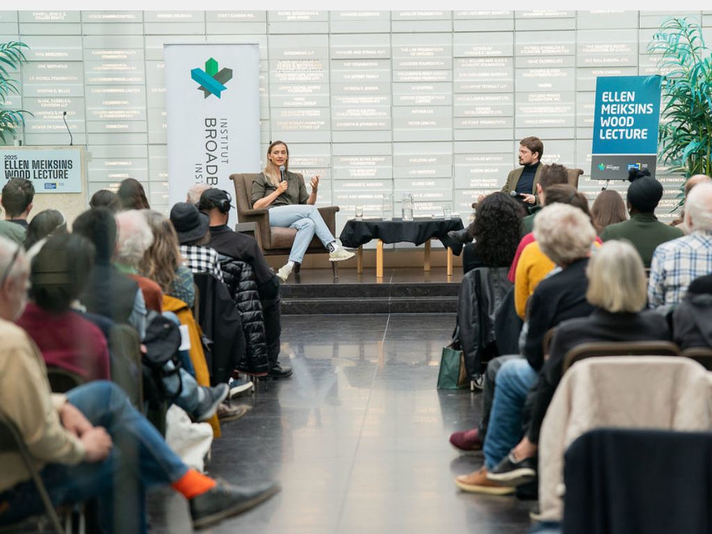 A group of people watching Grace Blakeley sitting down and talking with Luke Savage. 